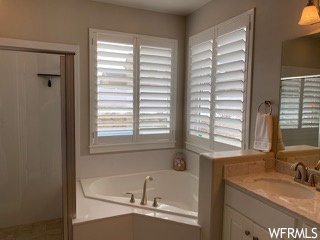 Bathroom with a healthy amount of sunlight, tiled tub, and vanity