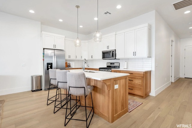 Kitchen with light wood-type flooring, hanging light fixtures, white cabinetry, and appliances with stainless steel finishes