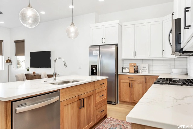 Kitchen with a center island with sink, appliances with stainless steel finishes, light wood-type flooring, white cabinets, and tasteful backsplash