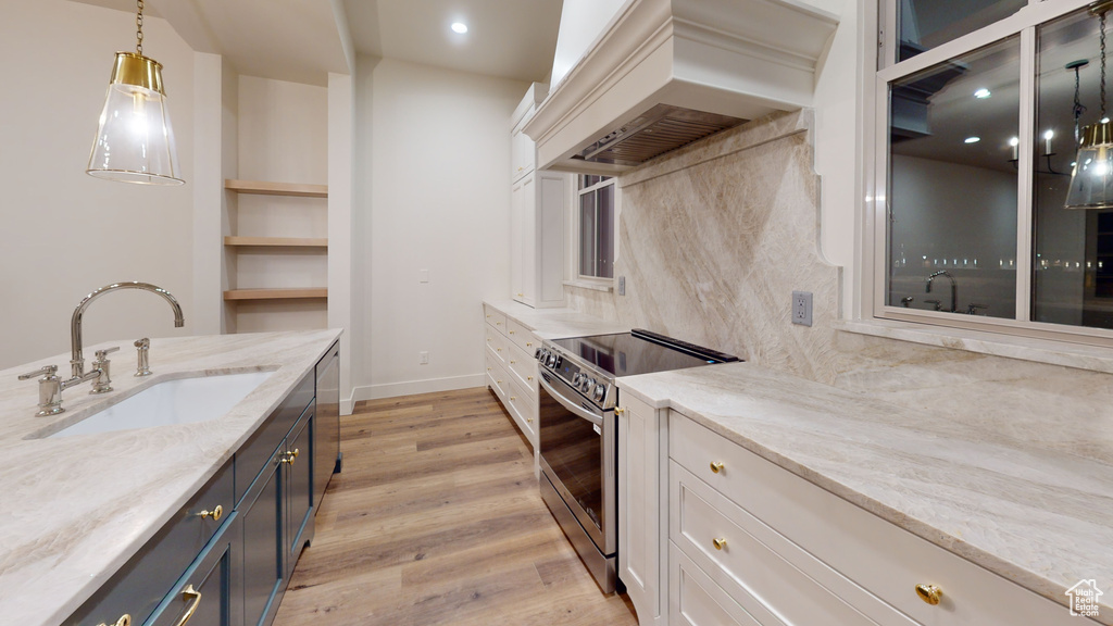 Kitchen featuring premium range hood, hanging light fixtures, sink, white cabinetry, and appliances with stainless steel finishes