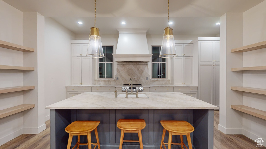 Kitchen with light wood-type flooring, light stone counters, white cabinets, and custom range hood