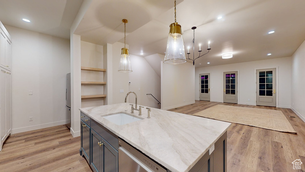 Kitchen with light stone countertops, a kitchen island with sink, decorative light fixtures, and light wood-type flooring