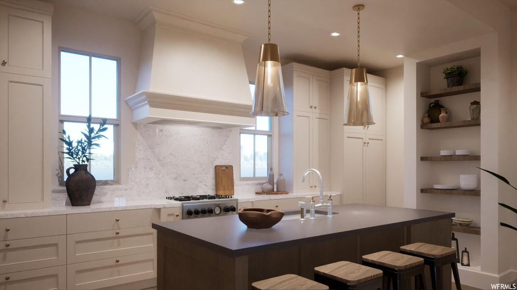 Kitchen featuring custom range hood, hanging light fixtures, a kitchen island with sink, tasteful backsplash, and a breakfast bar