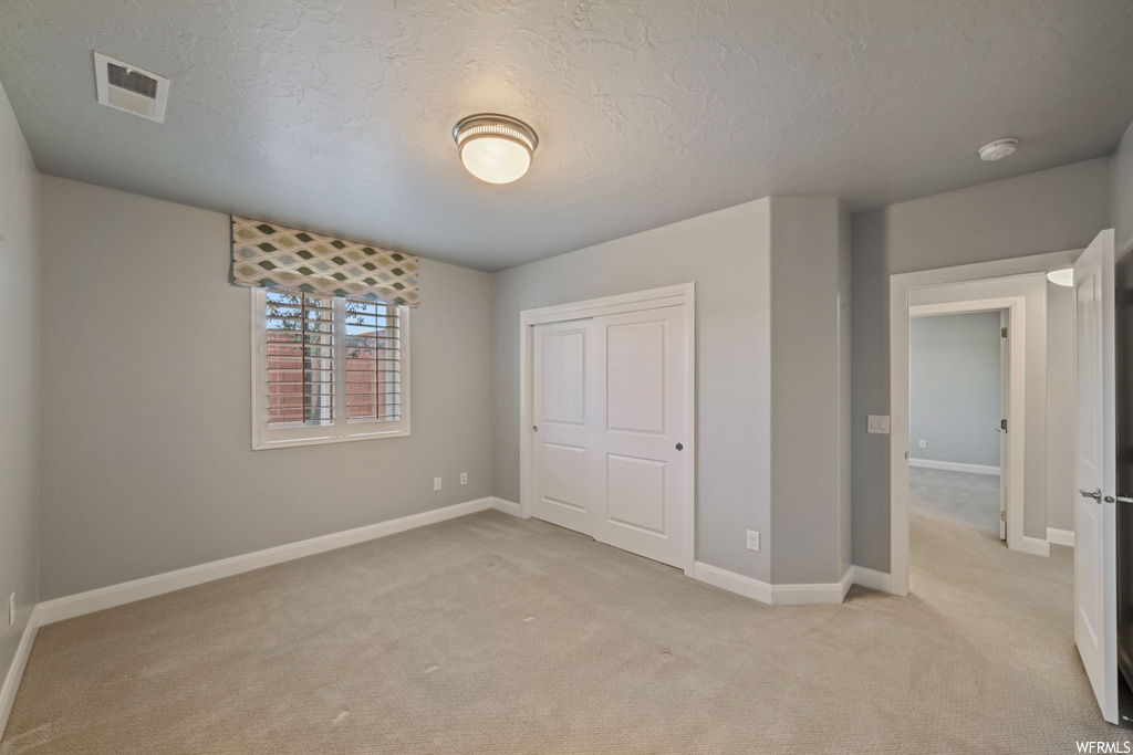 Unfurnished bedroom with light colored carpet, a textured ceiling, and a closet