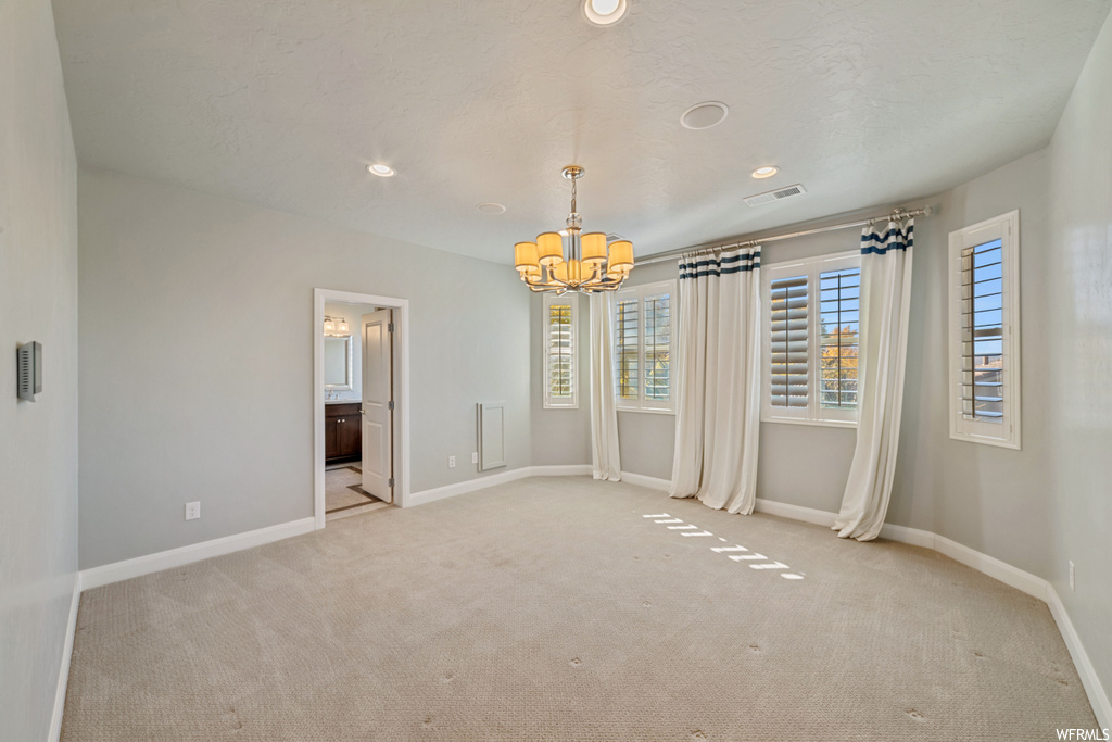 Spare room with light colored carpet and a notable chandelier