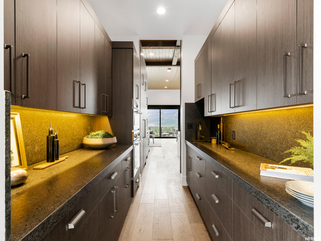 Kitchen featuring light hardwood / wood-style flooring, dark brown cabinets, oven, and backsplash