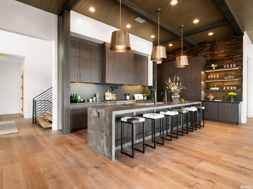 Kitchen featuring wood ceiling, light hardwood / wood-style floors, a kitchen bar, dark brown cabinetry, and backsplash
