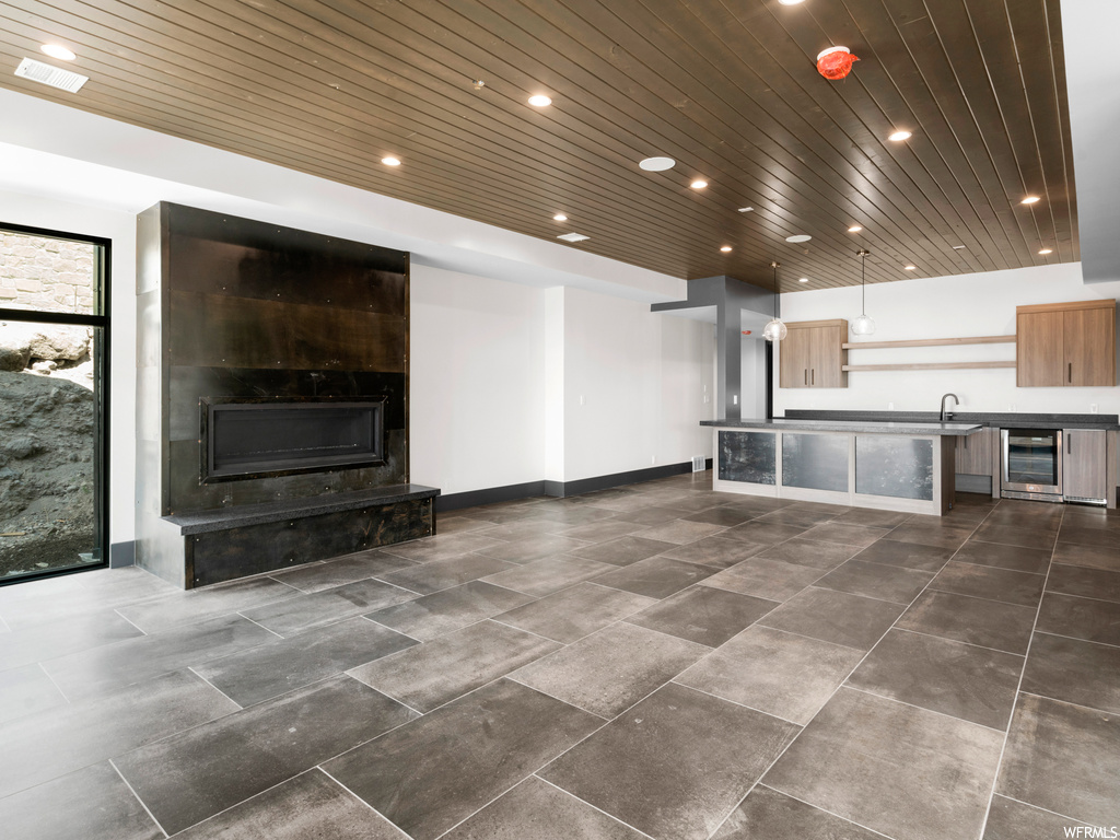 Unfurnished living room with a large fireplace, dark tile flooring, wooden ceiling, and wine cooler