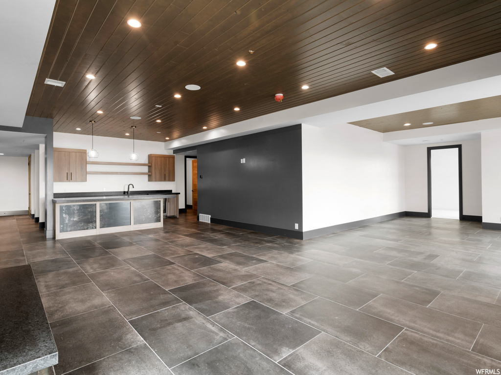 Unfurnished living room with dark tile floors, sink, and wood ceiling