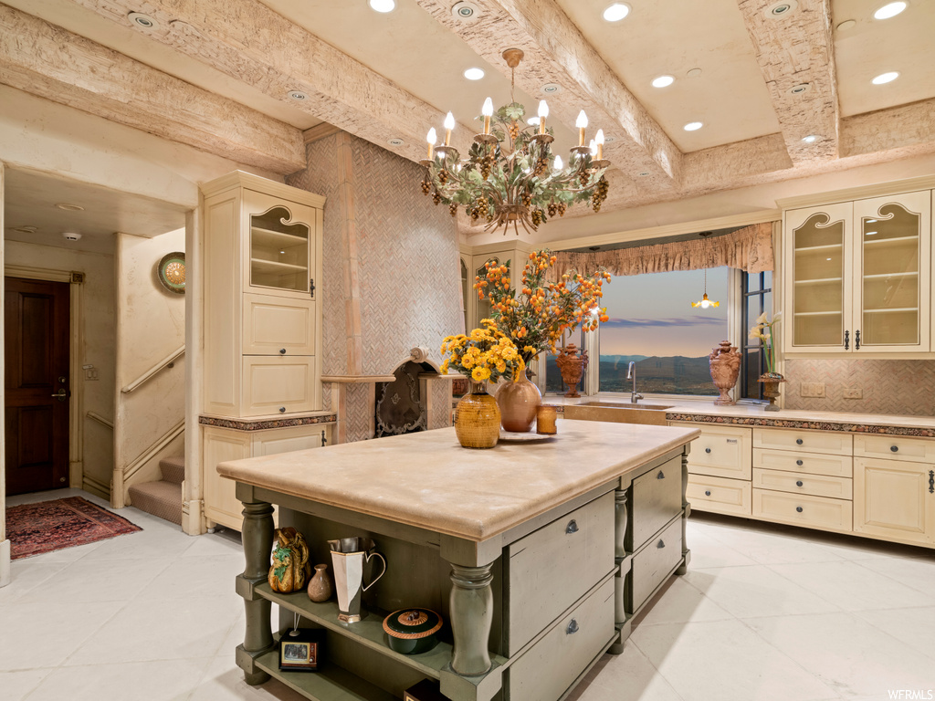 Kitchen with sink, beam ceiling, cream cabinets, a notable chandelier, and a kitchen island