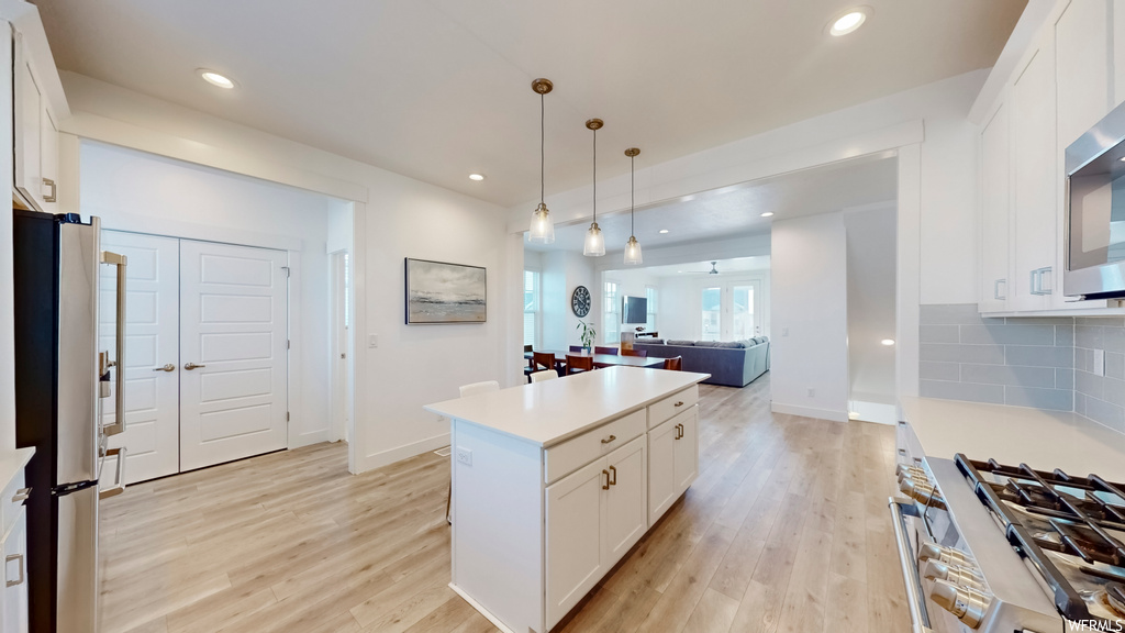 Kitchen featuring pendant lighting, tasteful backsplash, white cabinetry, light hardwood / wood-style flooring, and a kitchen island