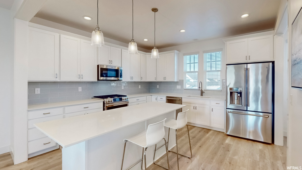 Kitchen with hanging light fixtures, light hardwood / wood-style floors, appliances with stainless steel finishes, backsplash, and white cabinetry