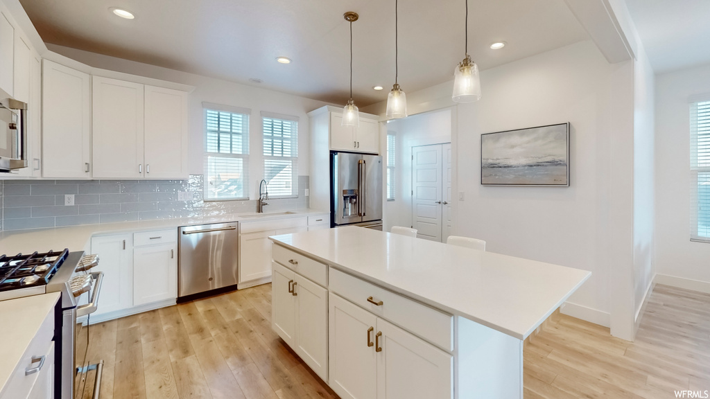 Kitchen with white cabinets, light wood-type flooring, premium appliances, and backsplash