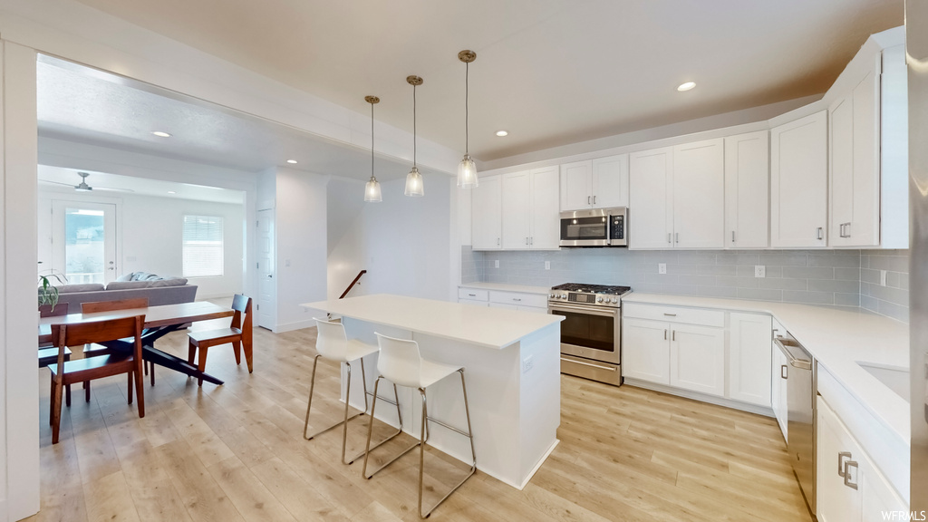 Kitchen featuring hanging light fixtures, appliances with stainless steel finishes, light hardwood / wood-style floors, tasteful backsplash, and white cabinetry