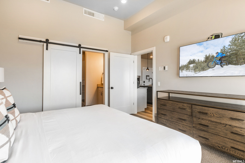 Bedroom with a closet, a barn door, ensuite bath, and light hardwood / wood-style floors