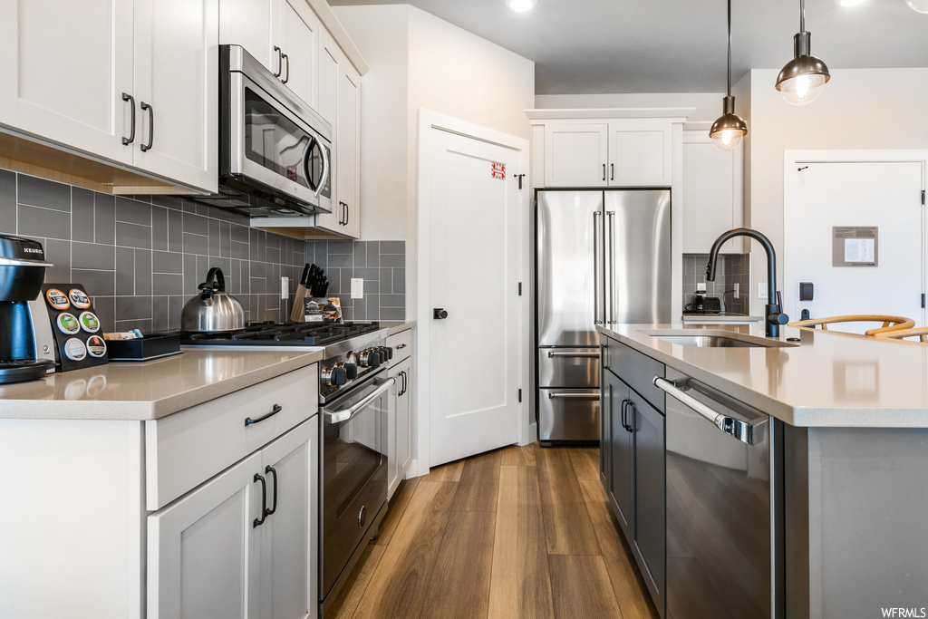Kitchen featuring dark wood-type flooring, high end appliances, pendant lighting, white cabinets, and backsplash