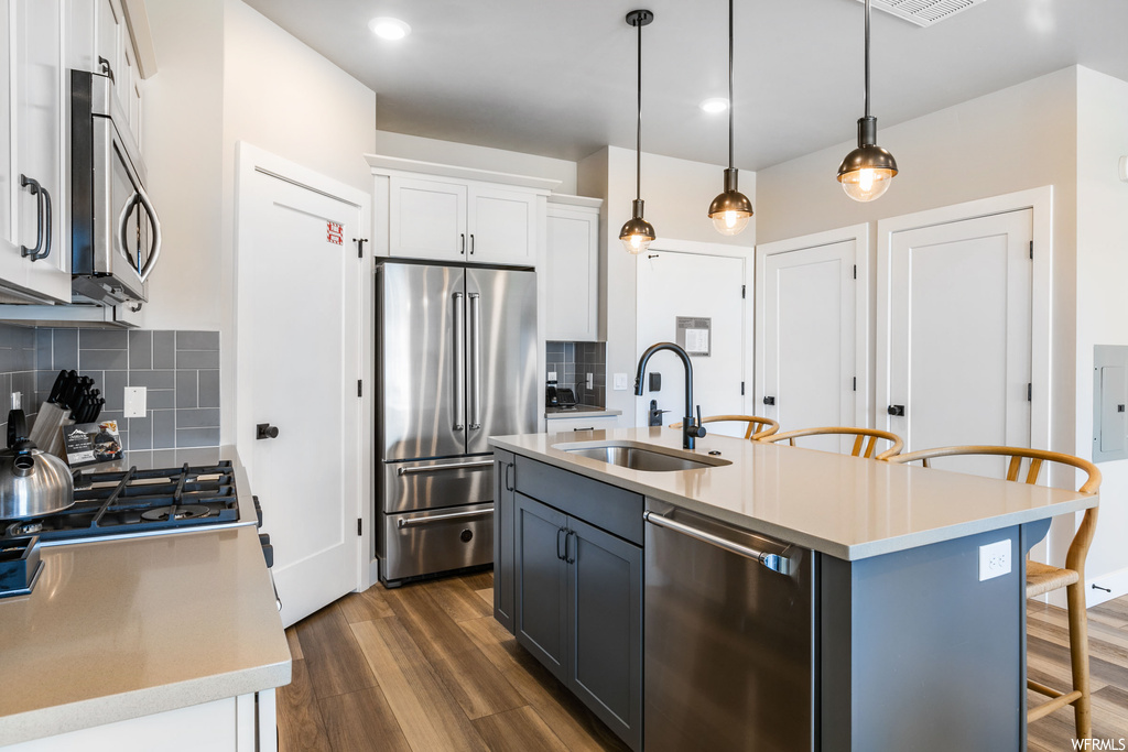 Kitchen featuring sink, appliances with stainless steel finishes, dark wood-type flooring, decorative light fixtures, and backsplash