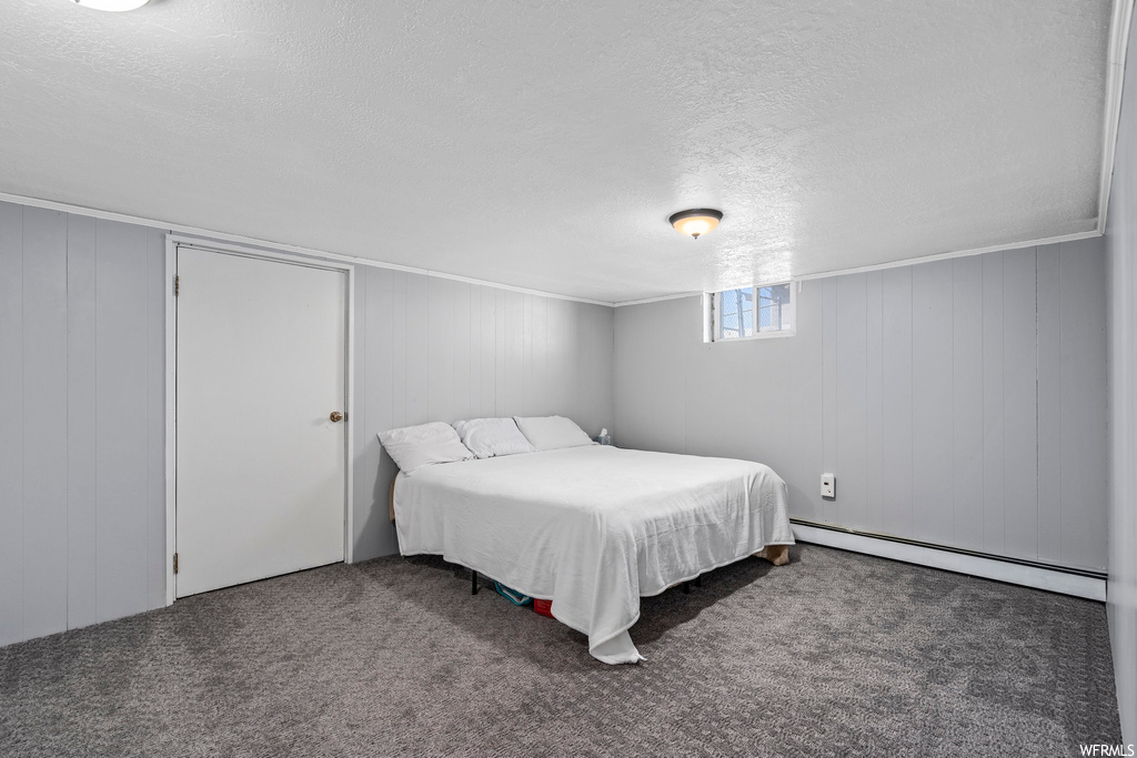 Bedroom featuring dark carpet, baseboard heating, a textured ceiling, and crown molding
