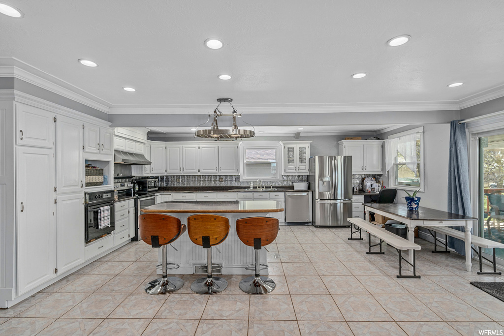Kitchen featuring a kitchen island, appliances with stainless steel finishes, tasteful backsplash, light tile floors, and white cabinetry