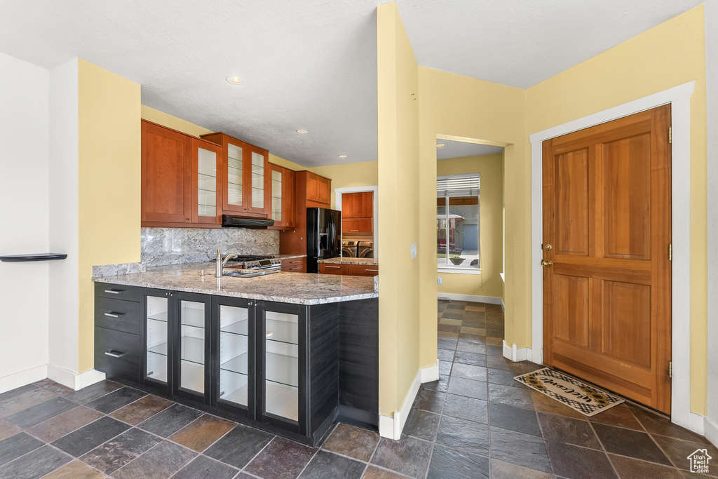Kitchen with tasteful backsplash, dark tile flooring, and light stone counters