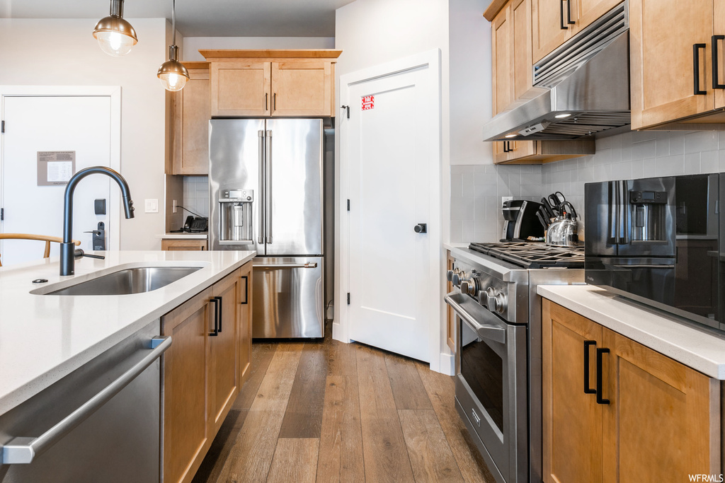 Kitchen with dark hardwood / wood-style flooring, sink, pendant lighting, high quality appliances, and tasteful backsplash