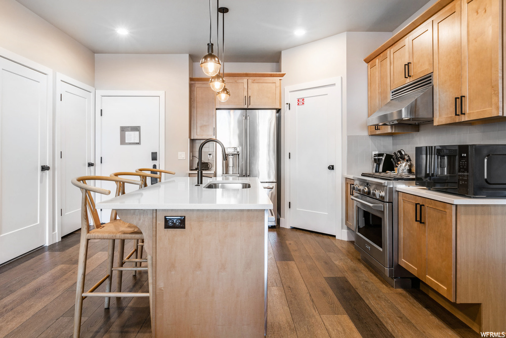 Kitchen featuring a center island with sink, dark wood-type flooring, tasteful backsplash, high end appliances, and decorative light fixtures