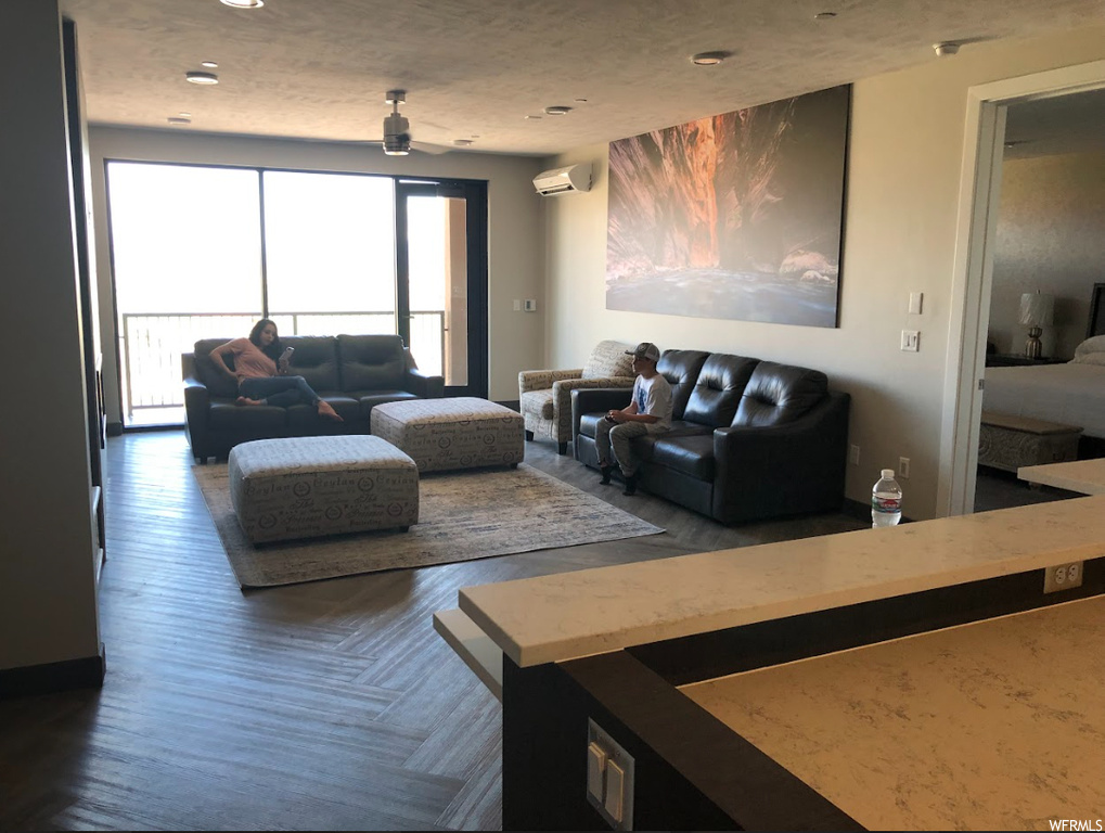 Living room with dark parquet floors, an AC wall unit, and a healthy amount of sunlight