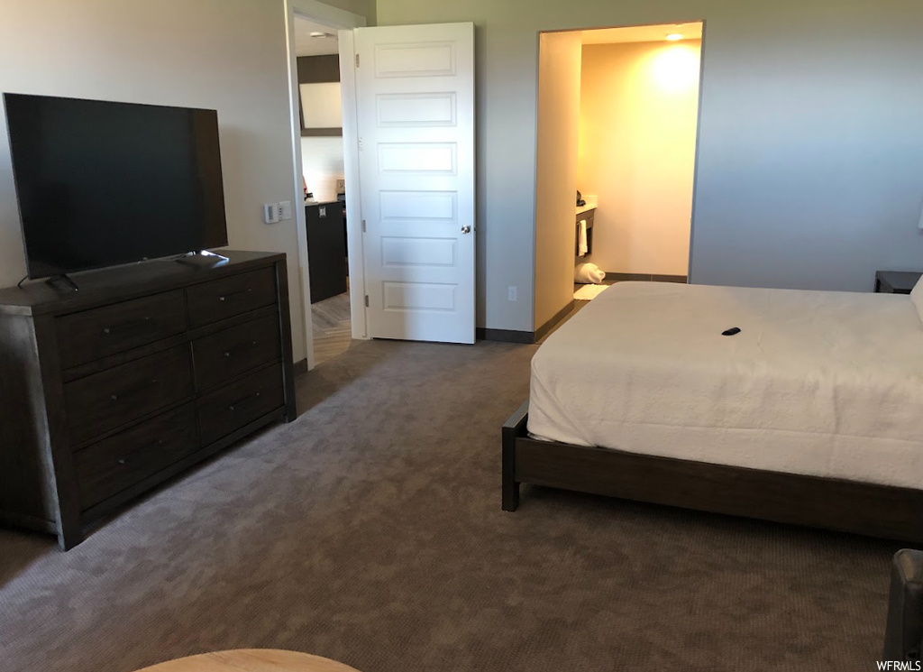 Bedroom with connected bathroom and dark colored carpet