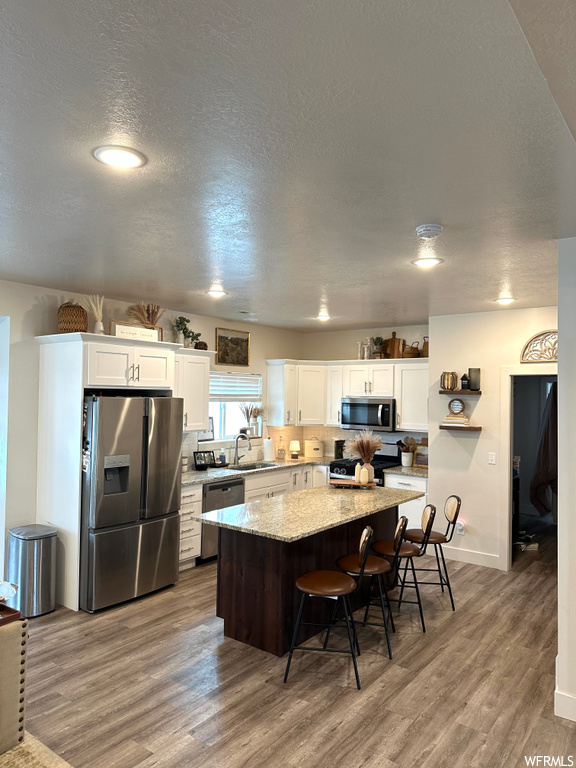 Kitchen with sink, hardwood / wood-style flooring, stainless steel appliances, white cabinets, and a kitchen island