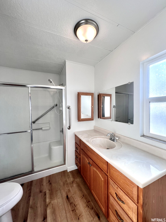 Bathroom featuring a shower with shower door, toilet, a textured ceiling, oversized vanity, and wood-type flooring