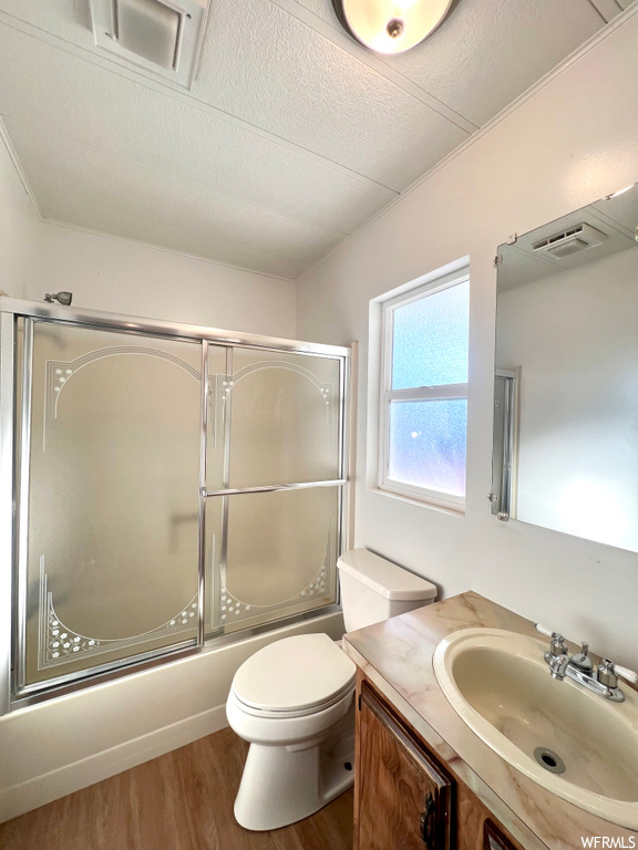 Full bathroom featuring toilet, enclosed tub / shower combo, a textured ceiling, vanity with extensive cabinet space, and wood-type flooring