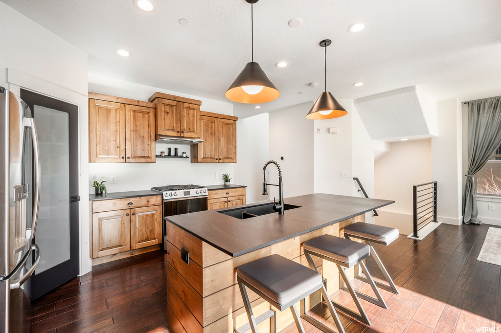 Kitchen featuring range with gas cooktop, hanging light fixtures, sink, a kitchen island with sink, and dark hardwood / wood-style flooring