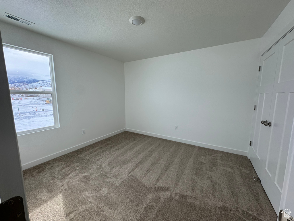 Empty room featuring a textured ceiling and dark colored carpet