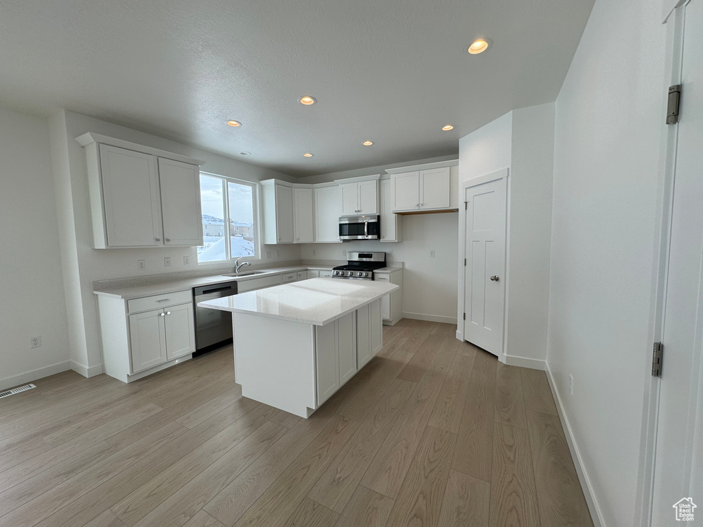 Kitchen featuring a kitchen island, appliances with stainless steel finishes, white cabinets, and light wood-type flooring