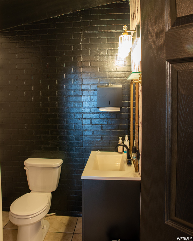 Bathroom with toilet, tile flooring, brick wall, lofted ceiling, and vanity