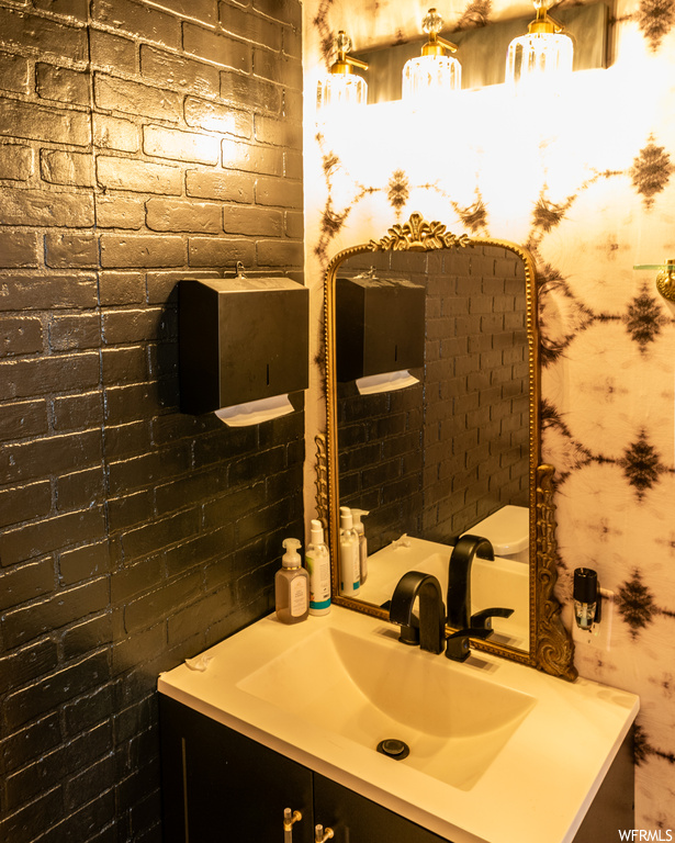Bathroom featuring toilet, brick wall, and vanity with extensive cabinet space