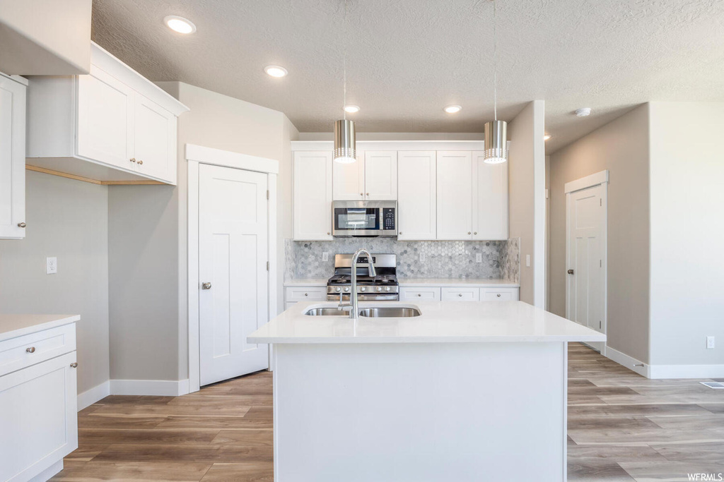 Kitchen featuring hanging light fixtures, light hardwood / wood-style floors, a kitchen island with sink, stainless steel appliances, and white cabinets