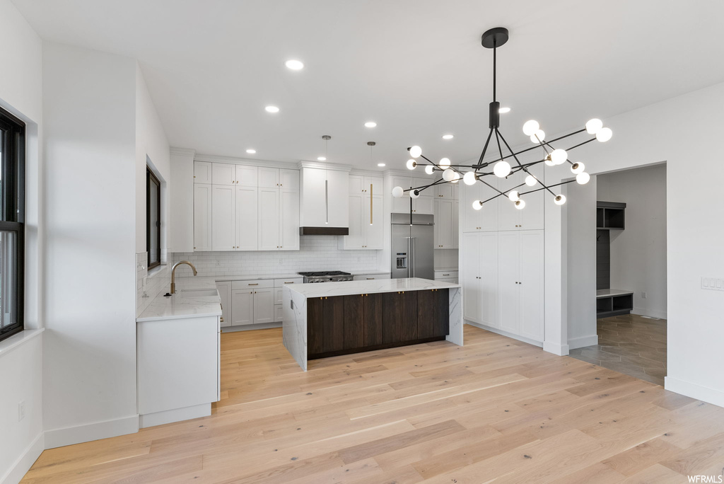 Kitchen with pendant lighting, an inviting chandelier, a kitchen island, built in fridge, and white cabinetry