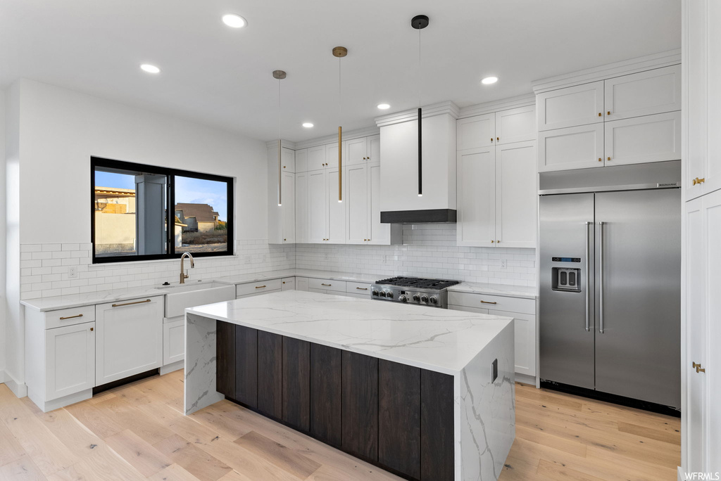 Kitchen with light hardwood / wood-style flooring, tasteful backsplash, stainless steel built in fridge, and white cabinetry