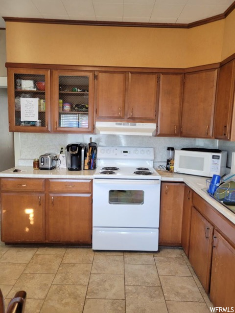 Kitchen with white appliances, backsplash, light tile flooring, and crown molding