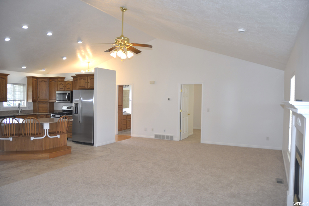 Kitchen with high vaulted ceiling, light colored carpet, a center island, stainless steel appliances, and ceiling fan