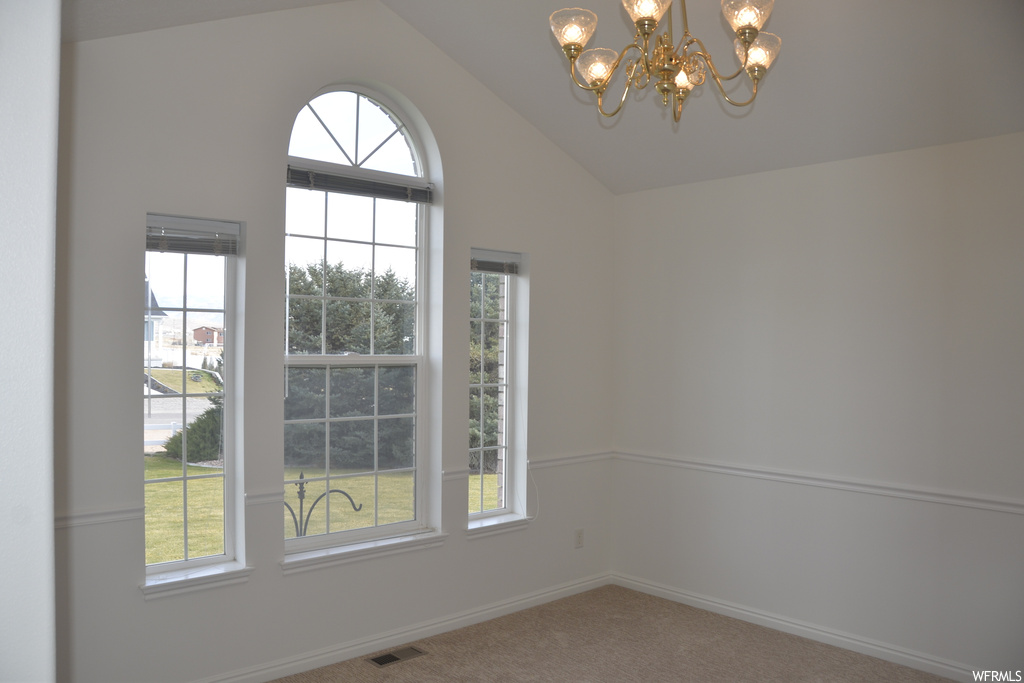 Unfurnished room with an inviting chandelier, vaulted ceiling, and carpet floors