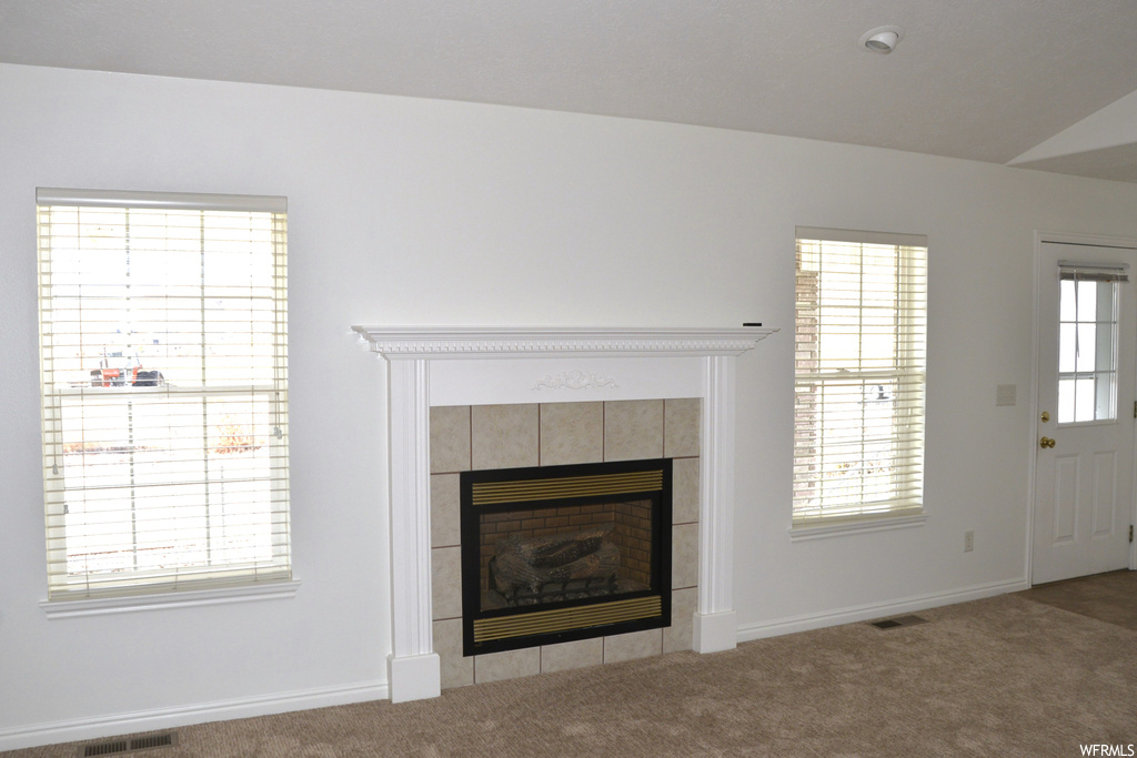 Unfurnished living room featuring a healthy amount of sunlight, a tile fireplace, and light colored carpet