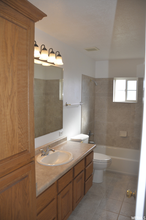 Full bathroom with tiled shower / bath, toilet, vanity with extensive cabinet space, and tile flooring