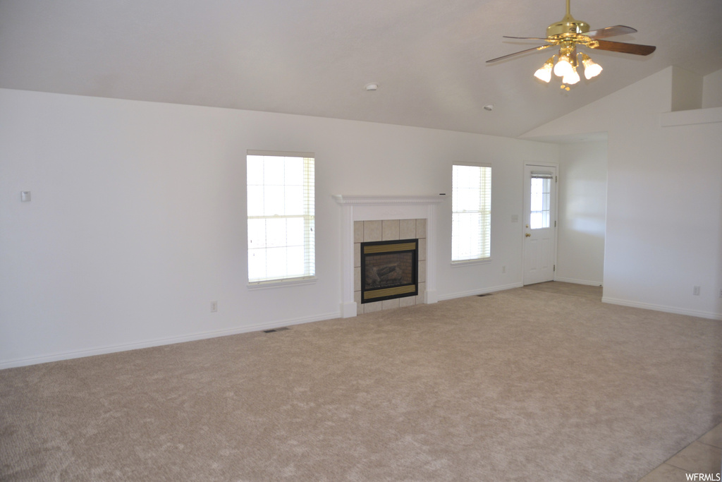 Unfurnished living room featuring ceiling fan, a fireplace, a healthy amount of sunlight, and vaulted ceiling