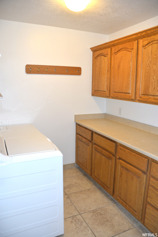 Laundry room featuring a textured ceiling, cabinets, and light tile floors