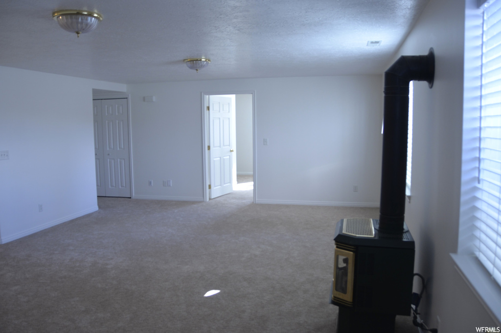 Unfurnished living room with a healthy amount of sunlight, a wood stove, and light colored carpet