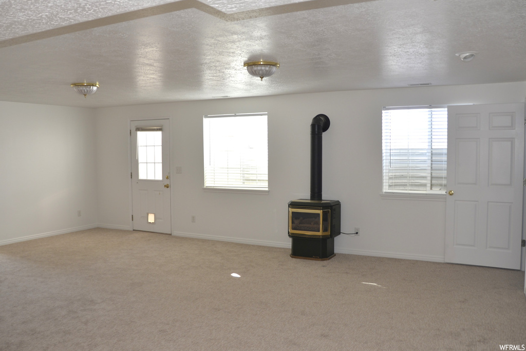 Unfurnished living room featuring light carpet, a wood stove, and a textured ceiling