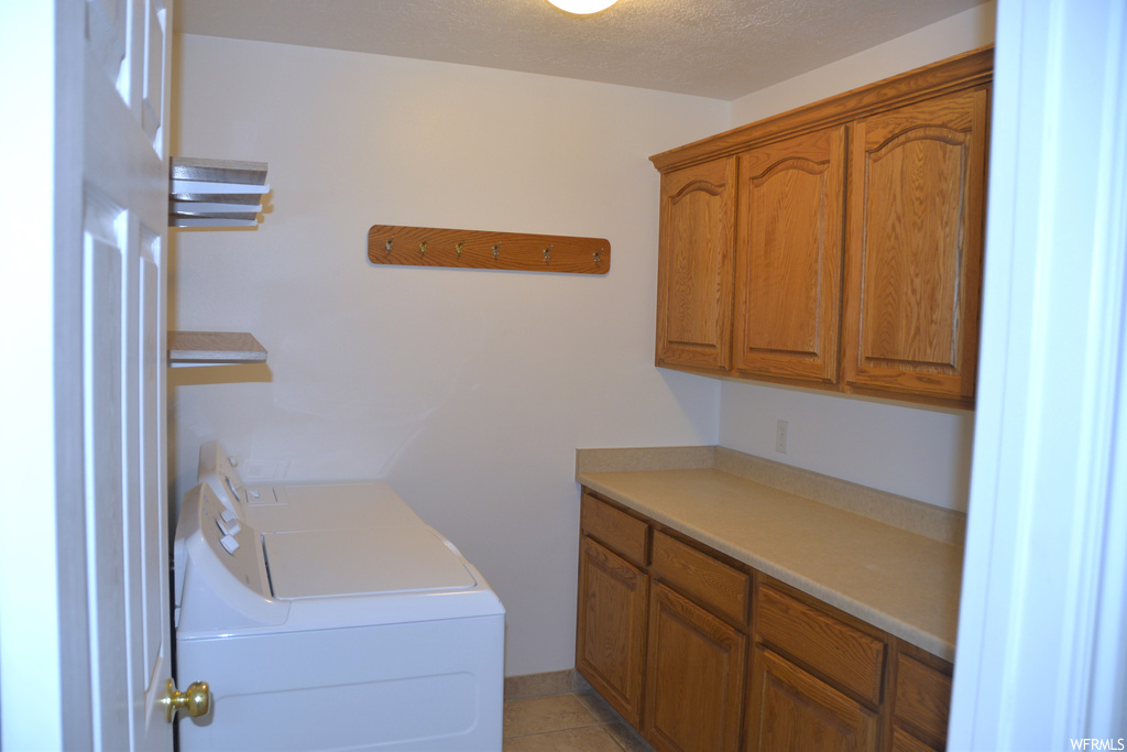 Clothes washing area with cabinets, washer and dryer, a textured ceiling, and light tile flooring