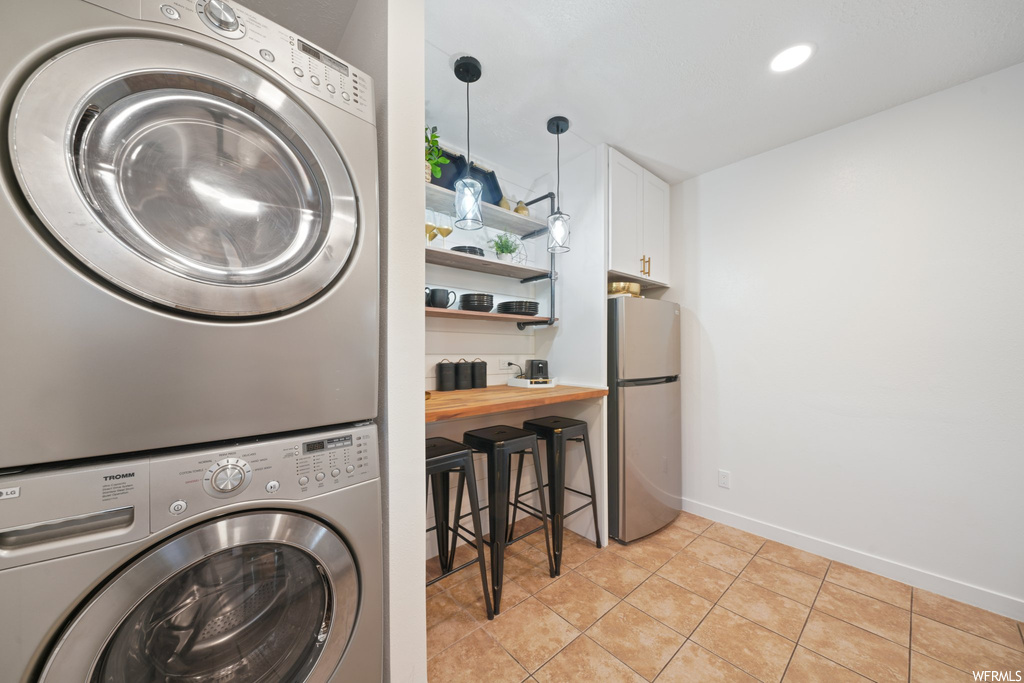 Clothes washing area with light tile floors and stacked washer and dryer